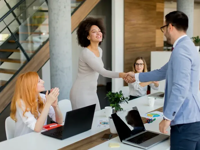 Smiling colleagues shake hands across a conference table in a bright office, celebrating a new listing partnership to help local clients